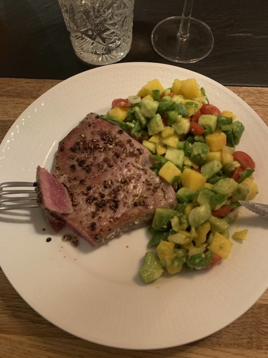 Medium-stekt tonfisk med svartpeppar och mangosalsa med avokado på vit tallrik.