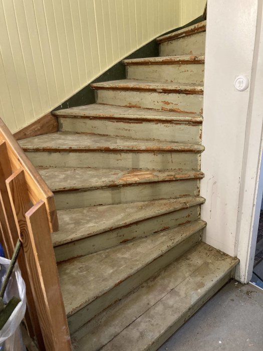 Gamla, slitna trätrappsteg och vitmålade trappräcken inne i ett hus.