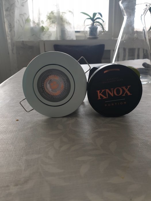 Infälld spotlight och en dosa snus på ett bord framför ett fönster.