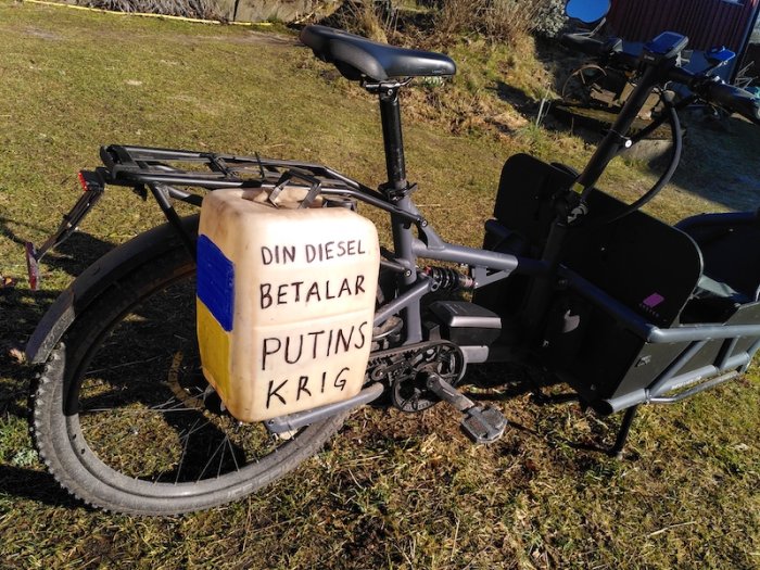 Lastcykel med en gammal dieseldunk dekorerad med texten "DIN DIESEL BETALAR PUTINS KRIG".