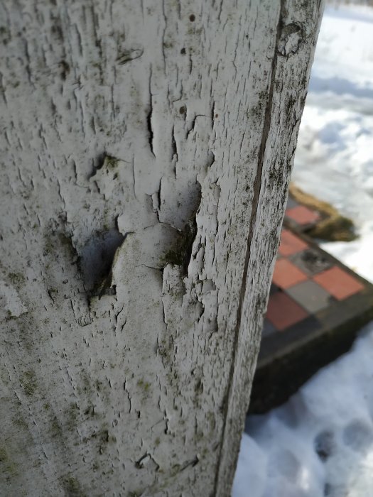 Närbild på slitet träbräde med flagande vit färg och sprickor, tecken på väderpåverkan.