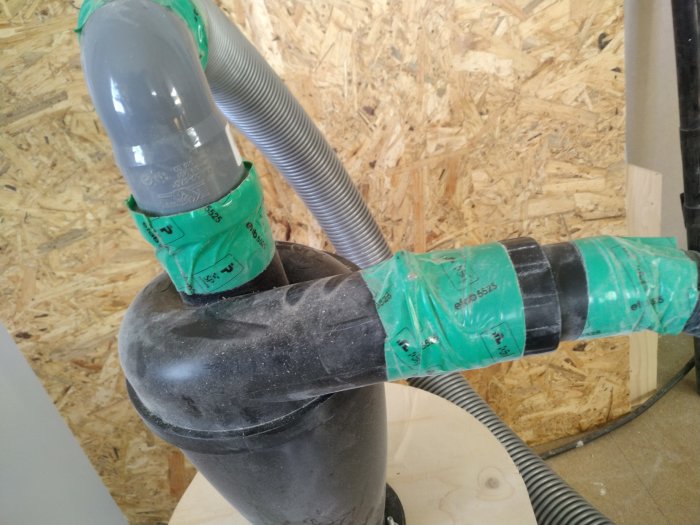 DIY dammsugarkoppling med grå och genomskinliga slangar förbundna med tejp på en byggarbetsplats.