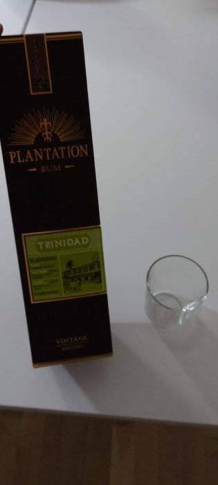 Flaska Plantation Rum i förpackning bredvid tomt glas på en vit yta.