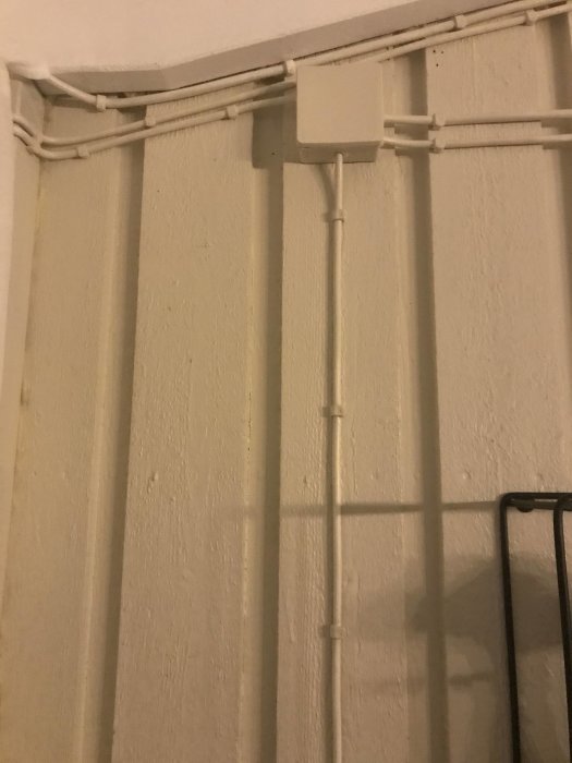 Kablage längs en vägg med hörn, där kablar är klamrade över lister och genom en plastkanal.