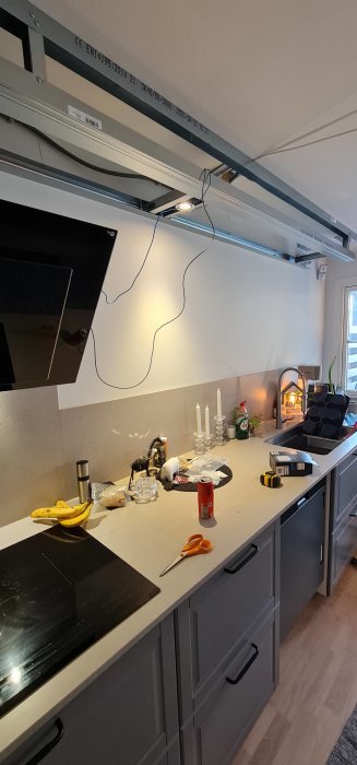 Kök under renovering med osammanhängande kablar och diverse föremål på bänkskivan.