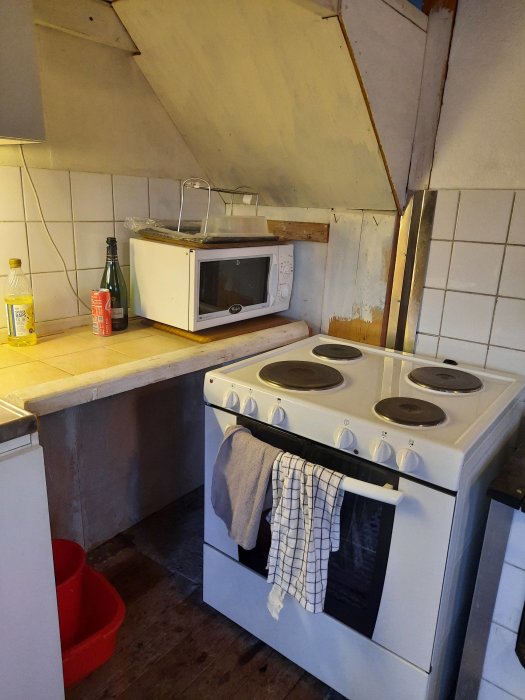 Ett orenoverat kökshörn med spis och mikrovågsugn under en sned trappavsats.