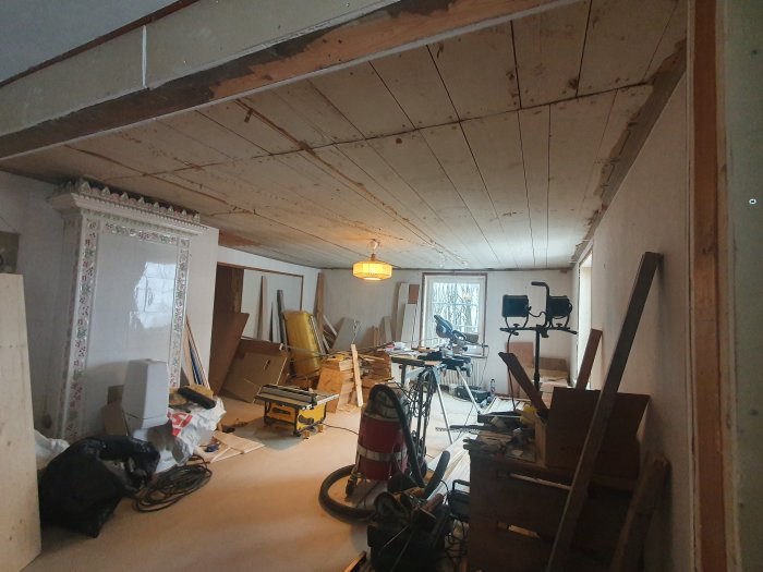 Renoveringsprojekt av ett rum med ojämnt träinnertak, verktyg och byggmaterial på golvet.
