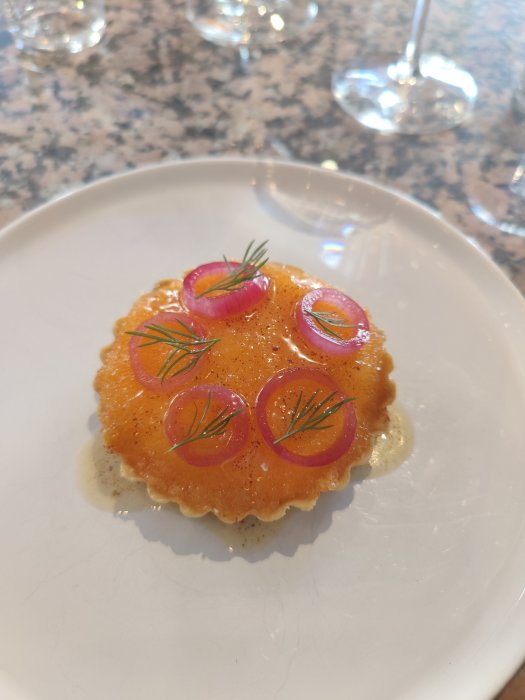 Löjroms tartlet med rödlöksringar och dill på en vit tallrik.