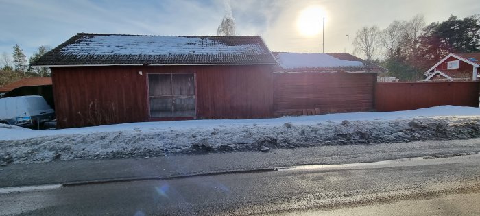 En gammal röd lada delvis täckt av snö vid sidan av en väg, efterfrågar målningsråd för renovering.