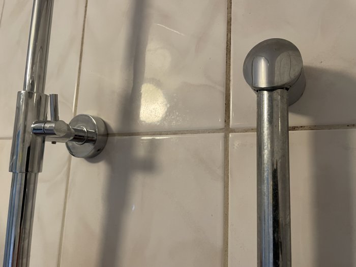 Duschstång och hållare monterad på kakelvägg, gammalt skruvhål syns.