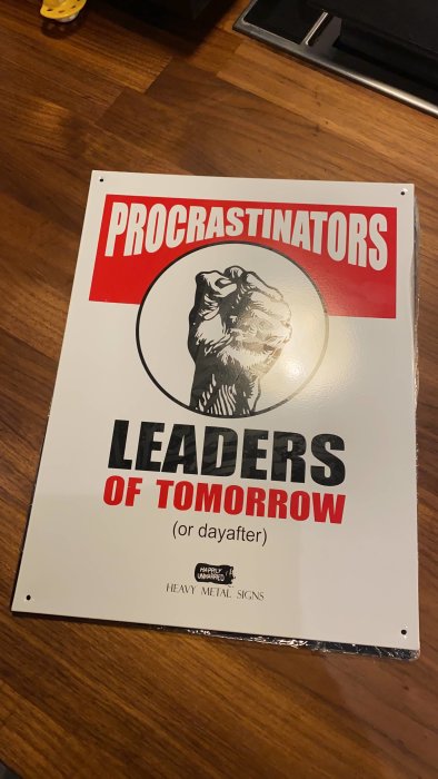 Skylt med texten "PROCRASTINATORS LEADERS OF TOMORROW (or day after)" och en silhuett av en liggande person.