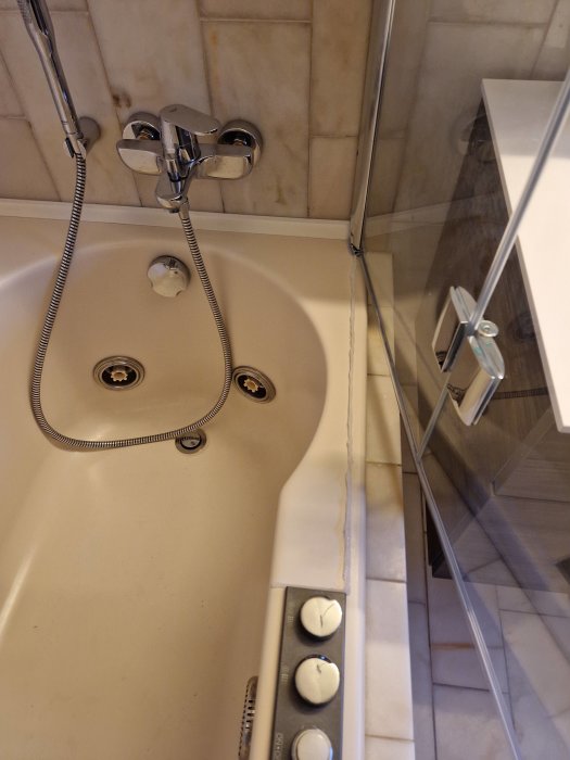 Översikt över ett badkar med synlig lutning och en ojämnt applicerad silikonfog längs kanten nära kakelvägg.