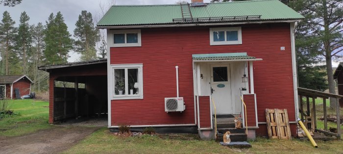 Rött tvåvåningshus med osymmetriskt utseende, inkluderande ett uterum och carport.