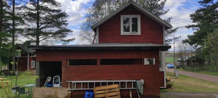 Rött hus med osymmetrisk tillbyggnad, uterum och carport under uppbyggnad.