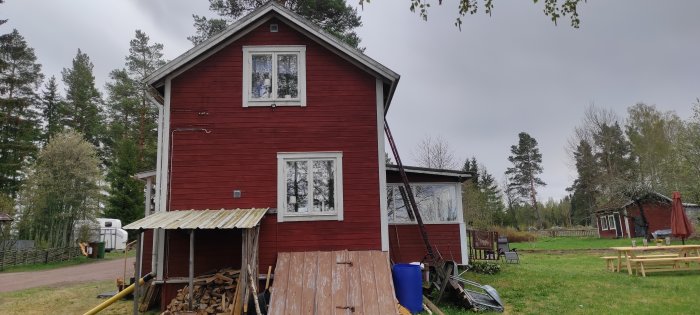 Tvåvåningshus med rött träslag, osymmetriskt med uterum och vedstapel.