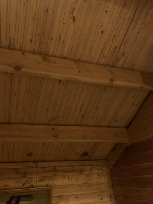 Exposed wooden beams and rafters in a stripped ceiling of a summer house, with visible electrical wiring.