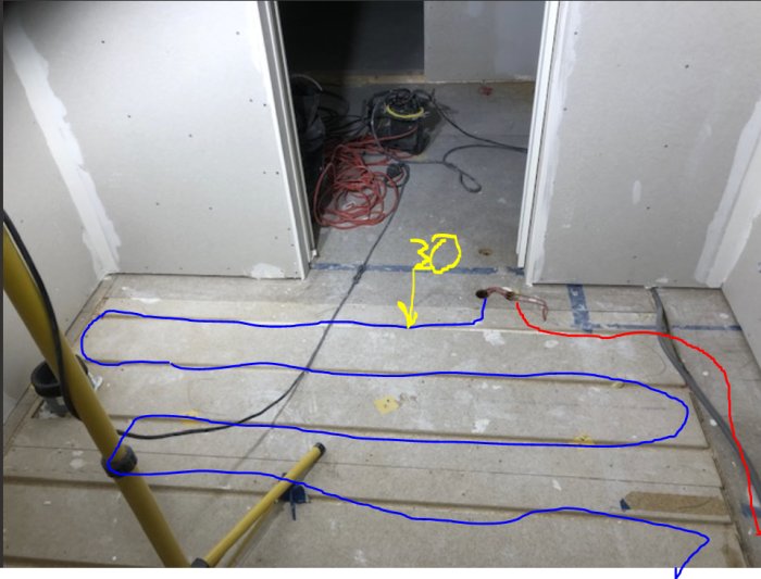 Golvvärmerör utlagda på betonggolv i badrum med planering markerad för fräsning nära dörröppning.