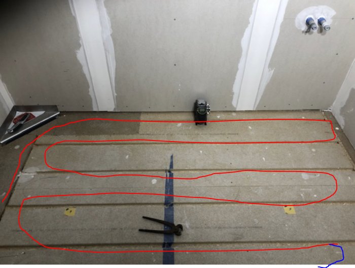 Installation av golvvärme med utmarkerade rörslingor på spånskiva, verktyg och mättejp syns, innan fräsning.