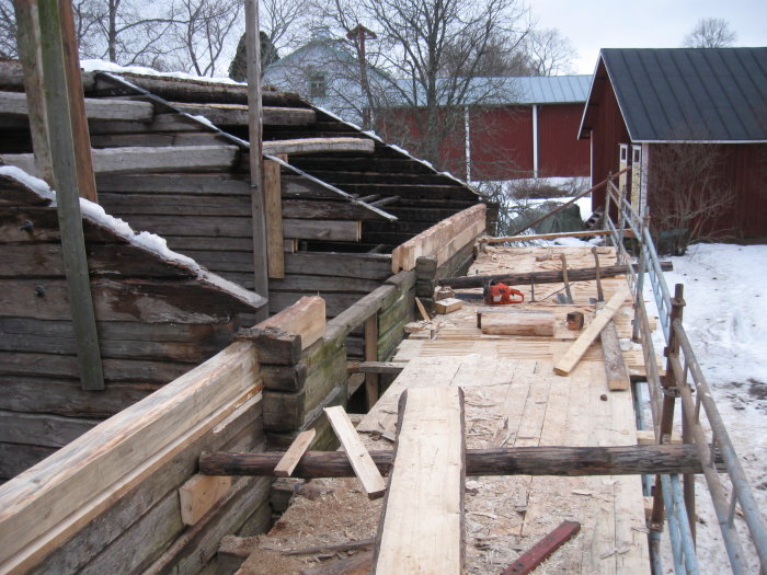 Reparation av en timrad byggnad med nya och gamla stockar synliga, arbetsredskap på en planka.