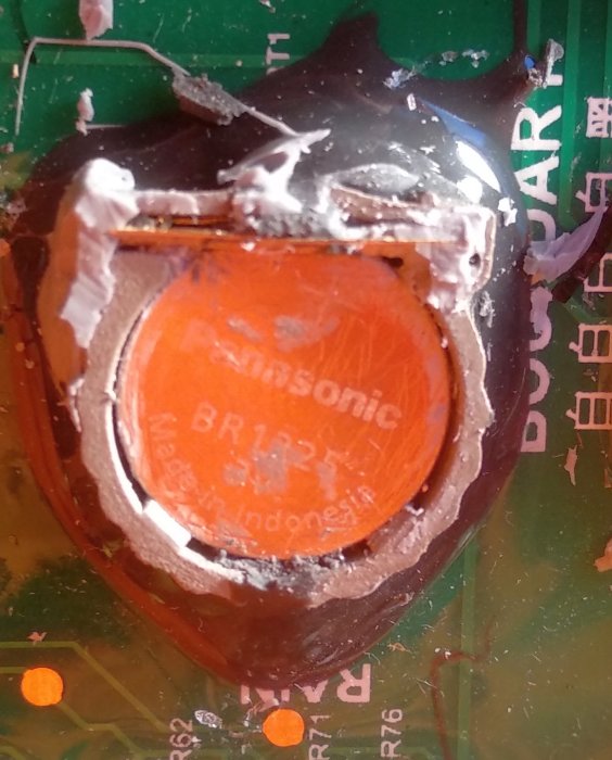 Närbild av ett Panasonic BR1225 batteri i hållare med rester av silikon runt det.