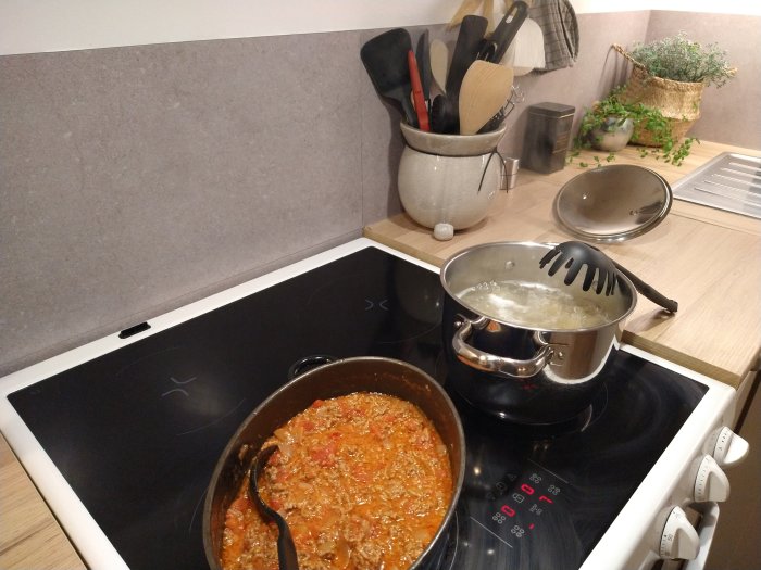 Köttfärssås i stekpanna och kokande makaroner på spis i ett modernt kök.