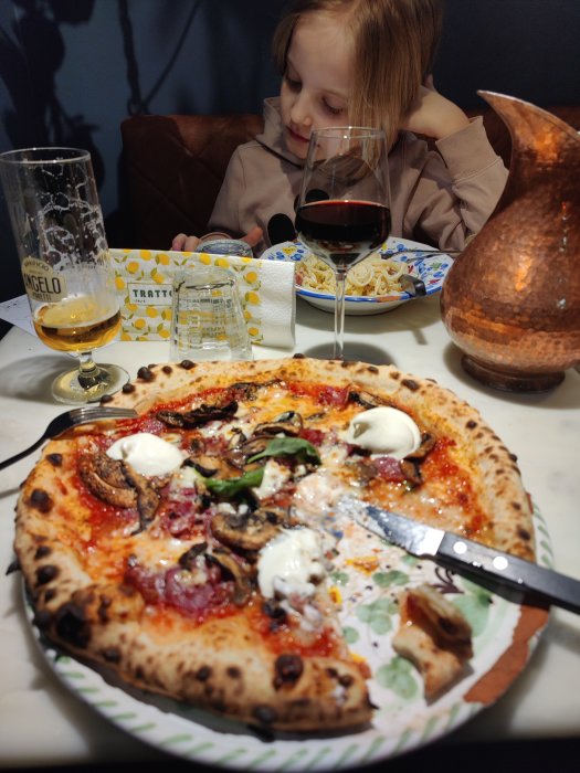 En halväten tryffelpizza på en tallrik framför ett barn och drycker på ett restaurangbord.