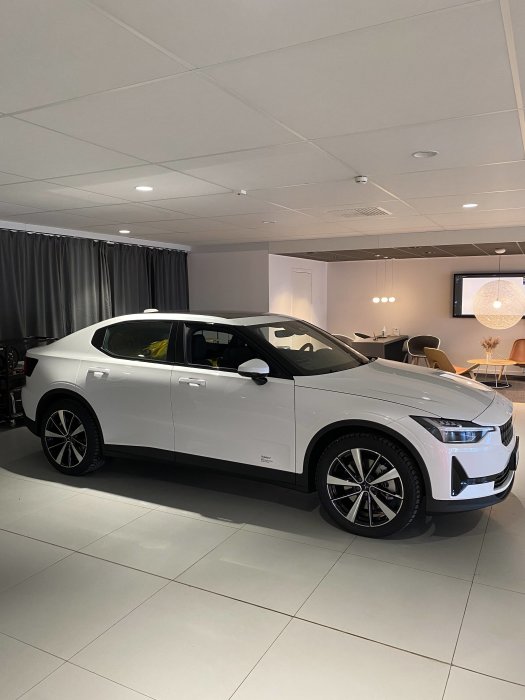 Vit elbil utställd i showroom med belysning och möbler i bakgrunden.