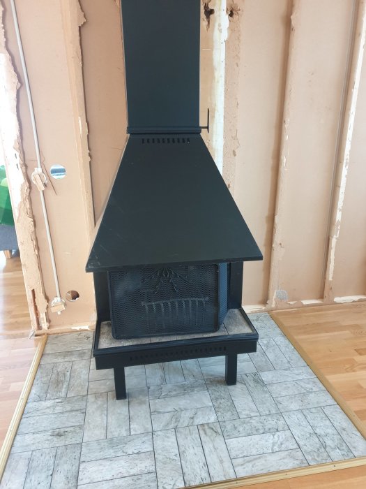 En traditionell svart öppen spis med skorstensrör står mot en vägg under renovering.