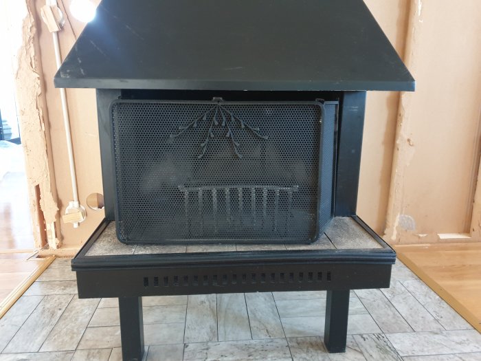 En gammal öppen spis i svart med metallskärm och askfångare, placerad i ett rum under renovering.