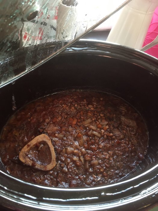 Osso buco som tillagas i en slowcooker, synligt benmärg och hackade grönsaker.