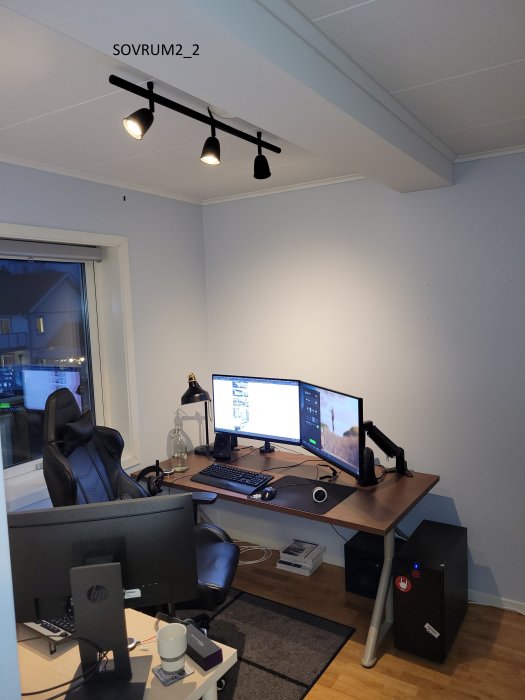 Kontorsrum med babyblå väggar, svart kontorsstol, skrivbord med datorskärmar och svart belysningsspår i taket.