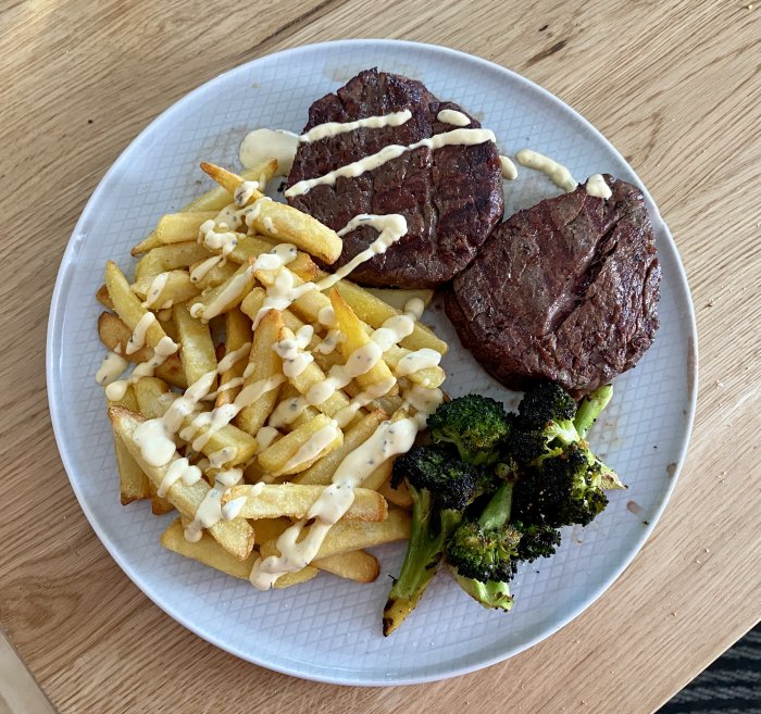 Grillad oxfilé med pommes frites och broccoli toppade med bearnaisesås på en tallrik.