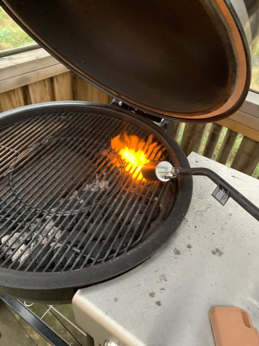 Weber Charcoal Summit grill med tända kol och öppet lock på en utomhusterrass.