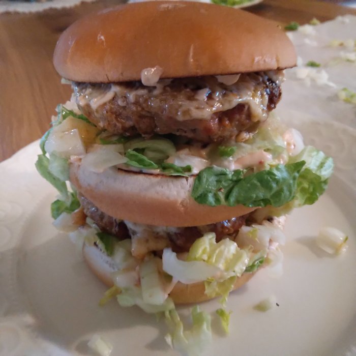 En stor dubbelhamburgare med sallad och dressing på en tallrik.