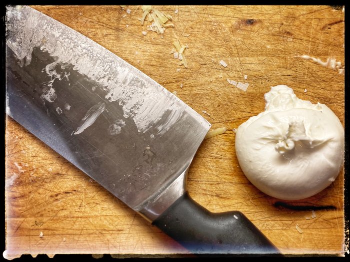 Burrataost bredvid en kökskniv på en använd skärbräda, redo för att toppa en pizza.