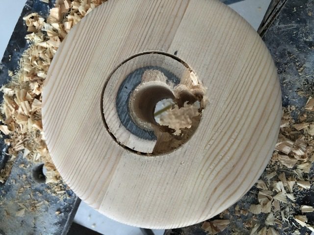 Rund limträskiva i furu på arbetsbord med uthuggen cirkel och träspån runtomkring.