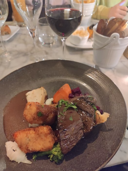 Renfilé på tallrik med potatis, morot och broccoli, glas rödvin i bakgrunden.