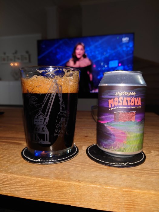 Ett glas med mörk stout och en ölburk från Stigbergets på ett bord, bakgrunden visar en suddig TV-skärm.