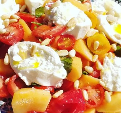 Burrata-melonsallad med tomater, basilika, pinjekärnor och rödpeppar, drizzlad med rapsolja.