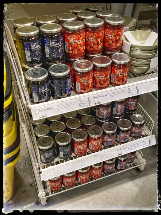Hyllor med olika syltburkar i en butik, inklusive jordgubbsylt och blåbärssylt, inte hjortronsylt.