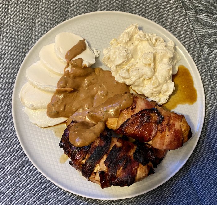 Baconinlindad kycklingfilé med brun sås, potatissallad, skivor av mozzarella och en skvätt bbq-sås på en tallrik.