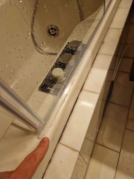 Närbild av delvis öppnad duschdörr med magnetlist längs kanten och vattendroppar, som visar effektivt vattentätningssystem.
