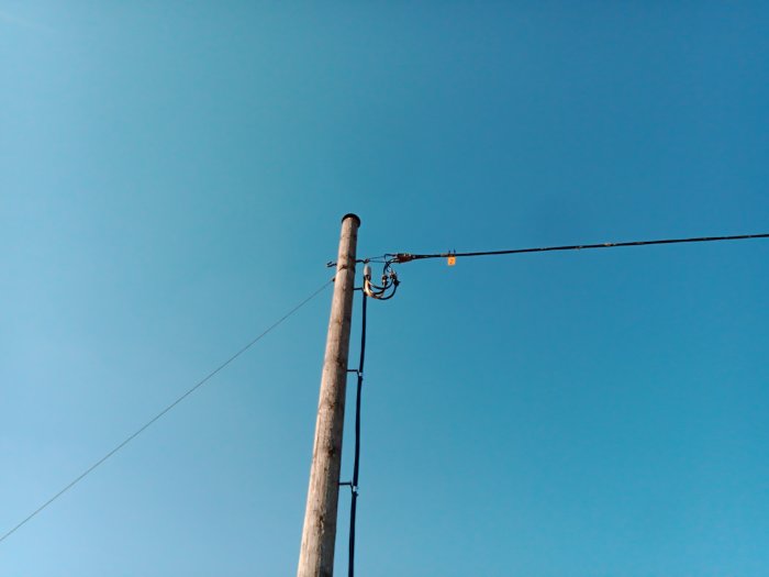 Elkabel hängande över en väg från en trästolpe mot en klarblå himmel.