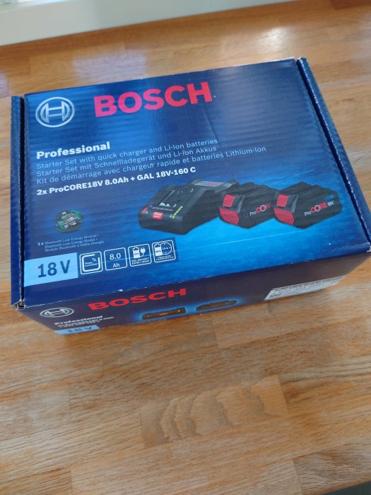 Bosch Professional snabbladdare och Li-ion batterier i förpackning på ett träbord.