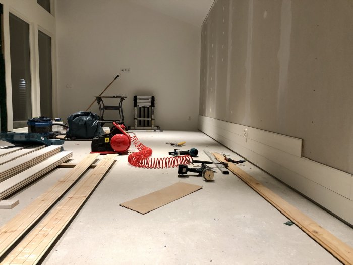 Renoveringsarbete med verktyg och träpaneler på ett golv i ett oinrett rum.