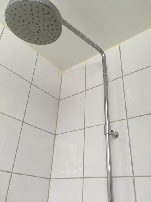 Väggmonterad handduschhållare i ett kaklat badrum med duschkoppen ovanför.