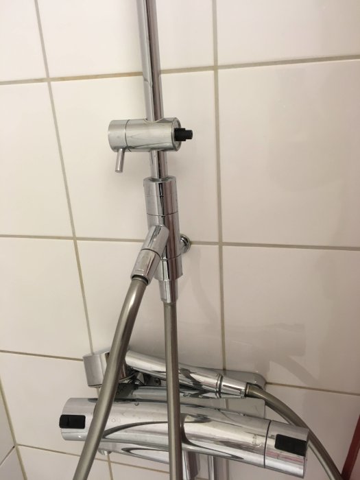 Handduschhållare monterad på metallstång mot kakelvägg som behöver tas bort för utbyte.