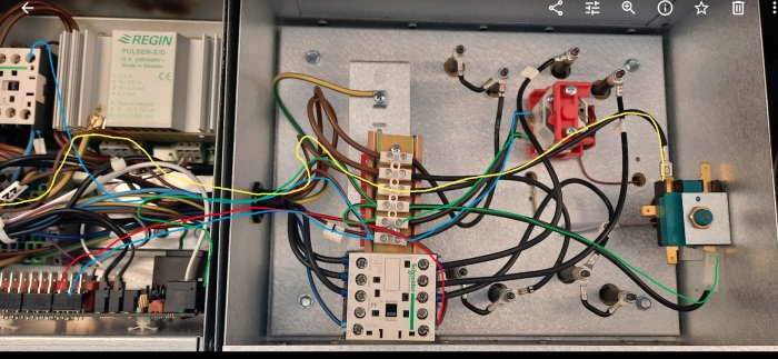 Komplex elpanel med flera termostater, kontrollkort och en kontraktor omgiven av många färgade kablar.