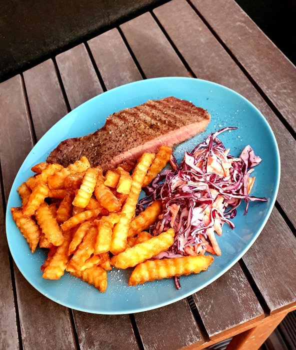 Grillad köttbit med kryddor, pommes frites och rödkålssallad på en blå tallrik.
