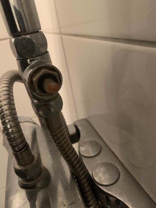 Duschblandare med saknat vred och ansluten duschslang mot kakelvägg.